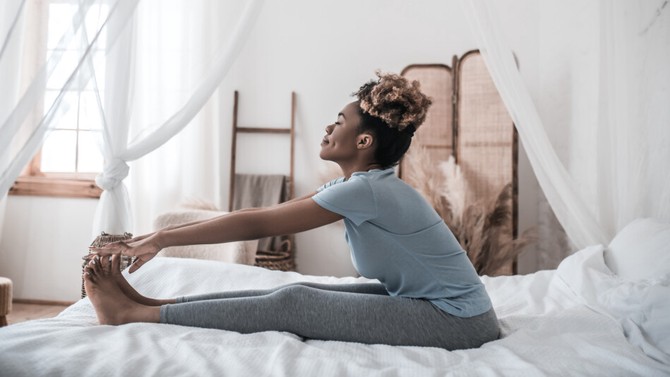 Black women doing yoga stretch in bed